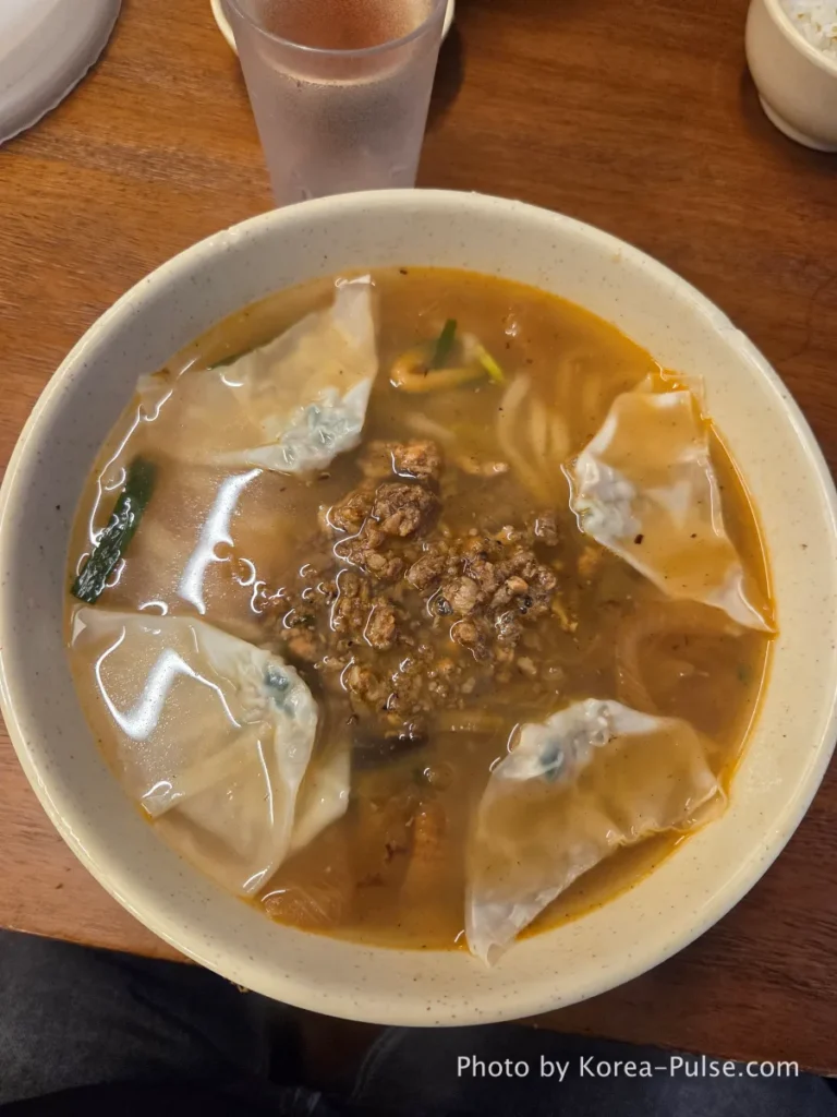 Best Myeongdong Restaurants: 5 Legendary Korean Spots Verified for 2026 2 A steaming bowl of Kalguksu (knife-cut noodles) with minced meat topping and four dumplings, alongside a plate of signature Mandu at Myeongdong Kyoza, recognized as one of the Best Myeongdong Restaurants.