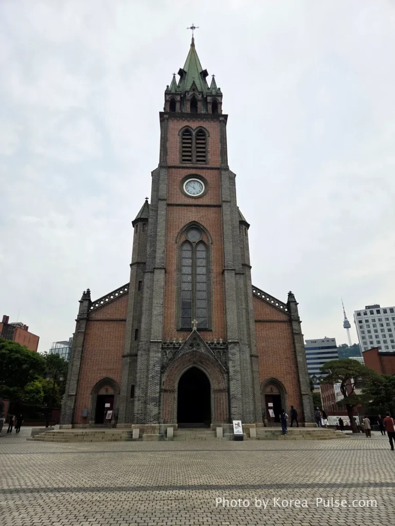 Myeongdong Cathedral: Seoul's Gothic Soul, Hidden Above the Shopping District 1 Full front facade of Myeongdong Cathedral Seoul — Gothic Revival red brick architecture with central bell tower rising 45 metres above the city