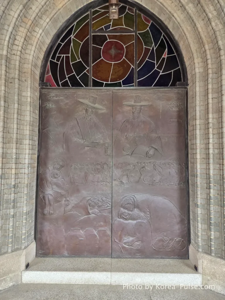 Myeongdong Cathedral: Seoul's Gothic Soul, Hidden Above the Shopping District 5 Main bronze entrance doors of Myeongdong Cathedral Seoul — intricate relief sculptures depicting Korean Catholic martyrs and early church history