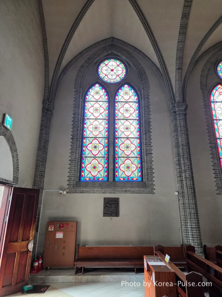 Myeongdong Cathedral: Seoul's Gothic Soul, Hidden Above the Shopping District 10 Tall lancet stained glass windows in Myeongdong Cathedral Seoul — colorful biblical scenes and geometric patterns in Gothic frames