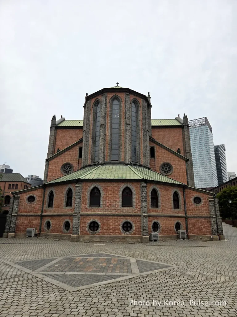 Myeongdong Cathedral: Seoul's Gothic Soul, Hidden Above the Shopping District 17 Exterior rear polygonal apse of Myeongdong Cathedral Seoul — brick Gothic Revival architecture surrounded by garden
