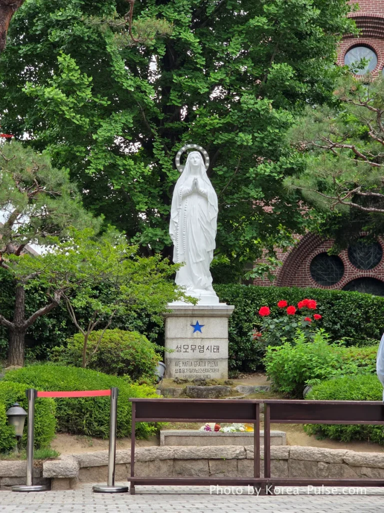 Myeongdong Cathedral: Seoul's Gothic Soul, Hidden Above the Shopping District 18 White marble statue of the Virgin Mary in stone grotto garden at the rear of Myeongdong Cathedral Seoul — Our Lady of the Immaculate Conception