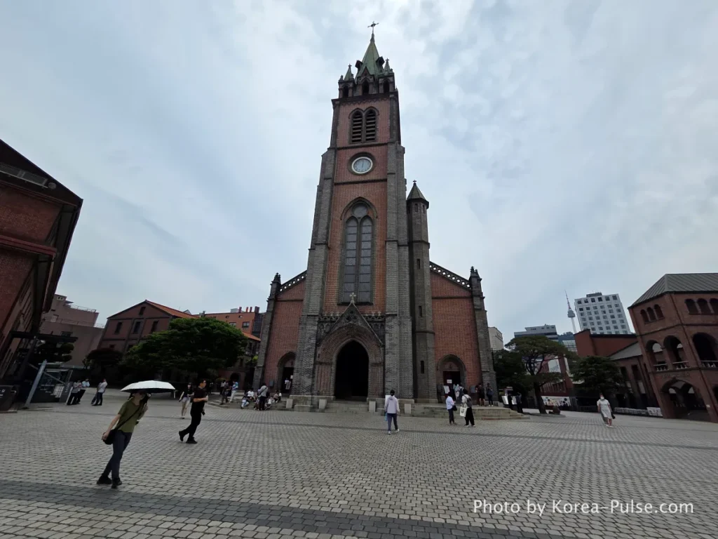 Myeongdong Cathedral: Seoul's Gothic Soul, Hidden Above the Shopping District 20 Myeongdong Cathedral front plaza with international visitors — Gothic facade and bell tower viewed from forecourt