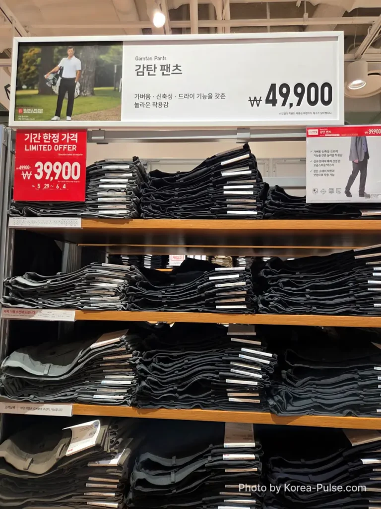 Uniqlo store display for the Gamtan Pants (감탄 팬츠), neatly stacked in dark charcoal and grey tones, with a red Limited Offer tag showing the sale price of 39,900 won reduced from 49,900 won