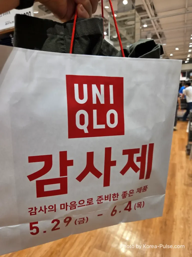 A Uniqlo paper shopping bag printed with the bold red Gamsaje 감사제 branding and sale dates May 29 to June 4, held up inside the store
