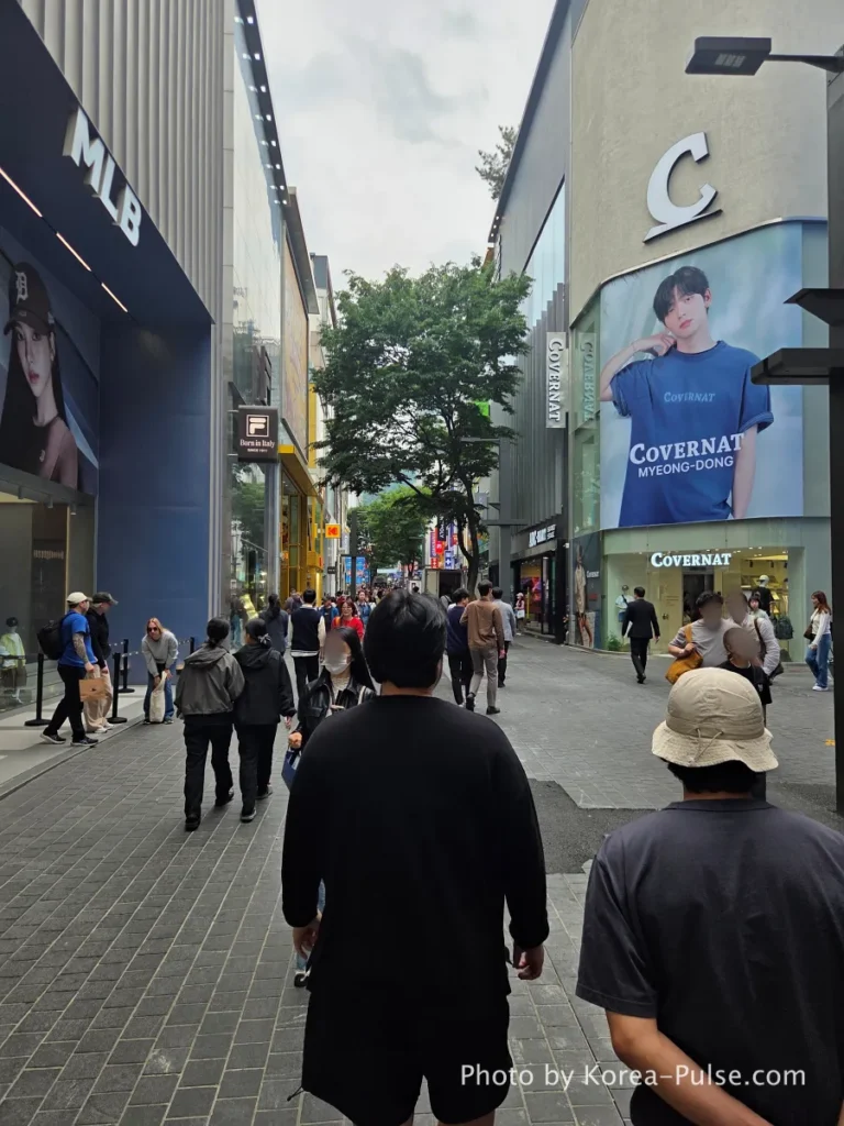 Myeongdong shopping street with MLB and Covernat brand stores, pedestrians walking through tree-lined avenue in May