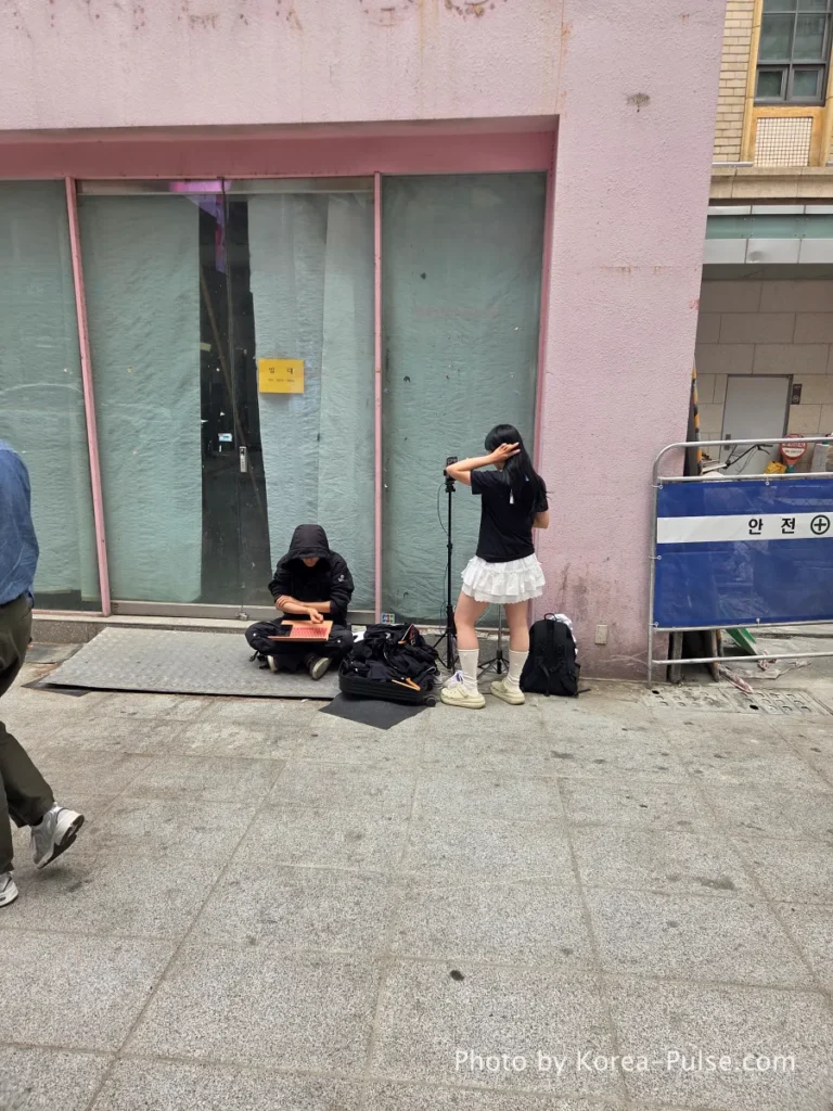 Female content creator live streaming outdoors in Myeongdong street while male crew member manages broadcasting equipment on the pavement