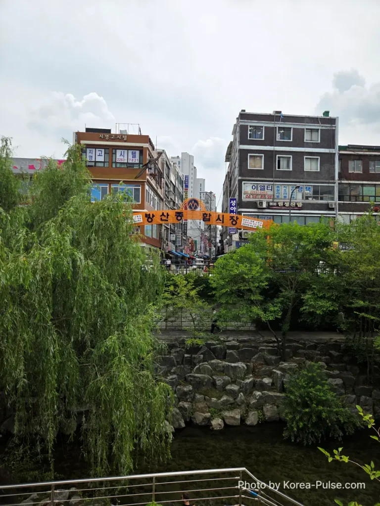 Gwangjang Market Seoul: The Complete Entry Guide — Part 1 7 View across Cheonggyecheon stream from near South Gate 1 of Gwangjang Market toward the orange Bangsan Market sign