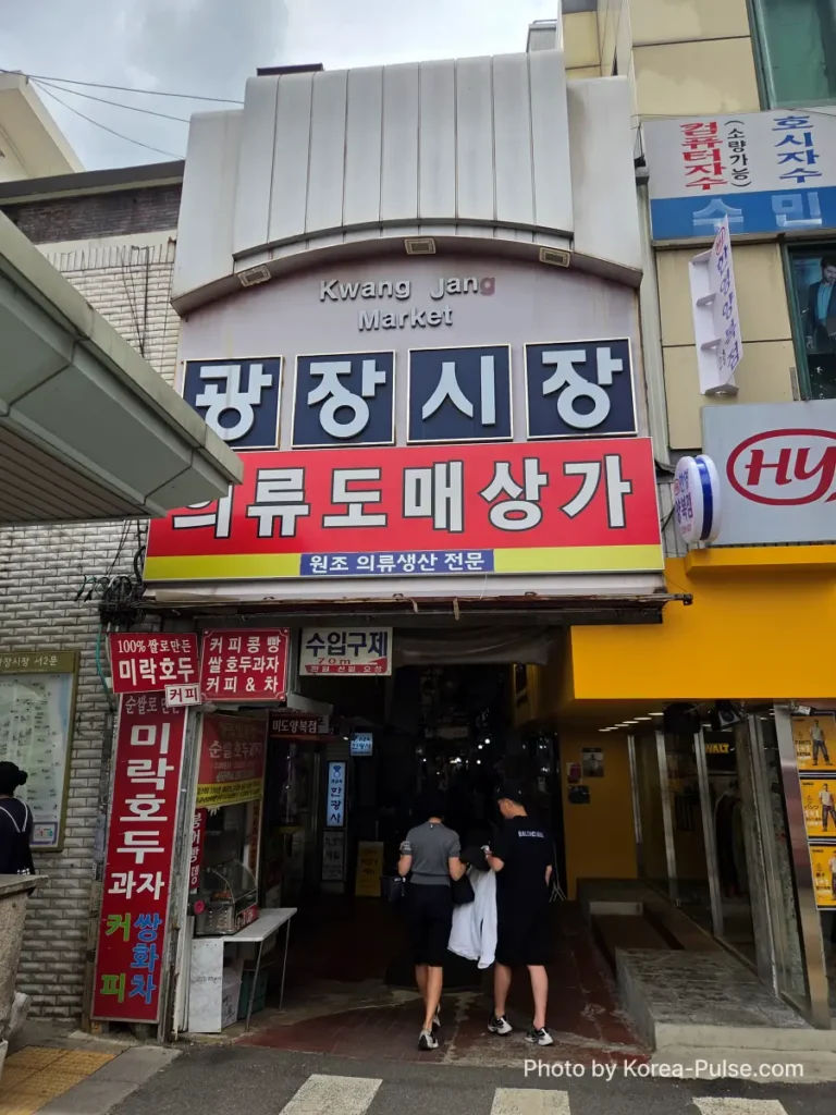 Gwangjang Market Seoul: The Complete Entry Guide — Part 1 9 West Gate 2 smaller entrance of Gwangjang Market Seoul with 광장시장 sign and two people entering