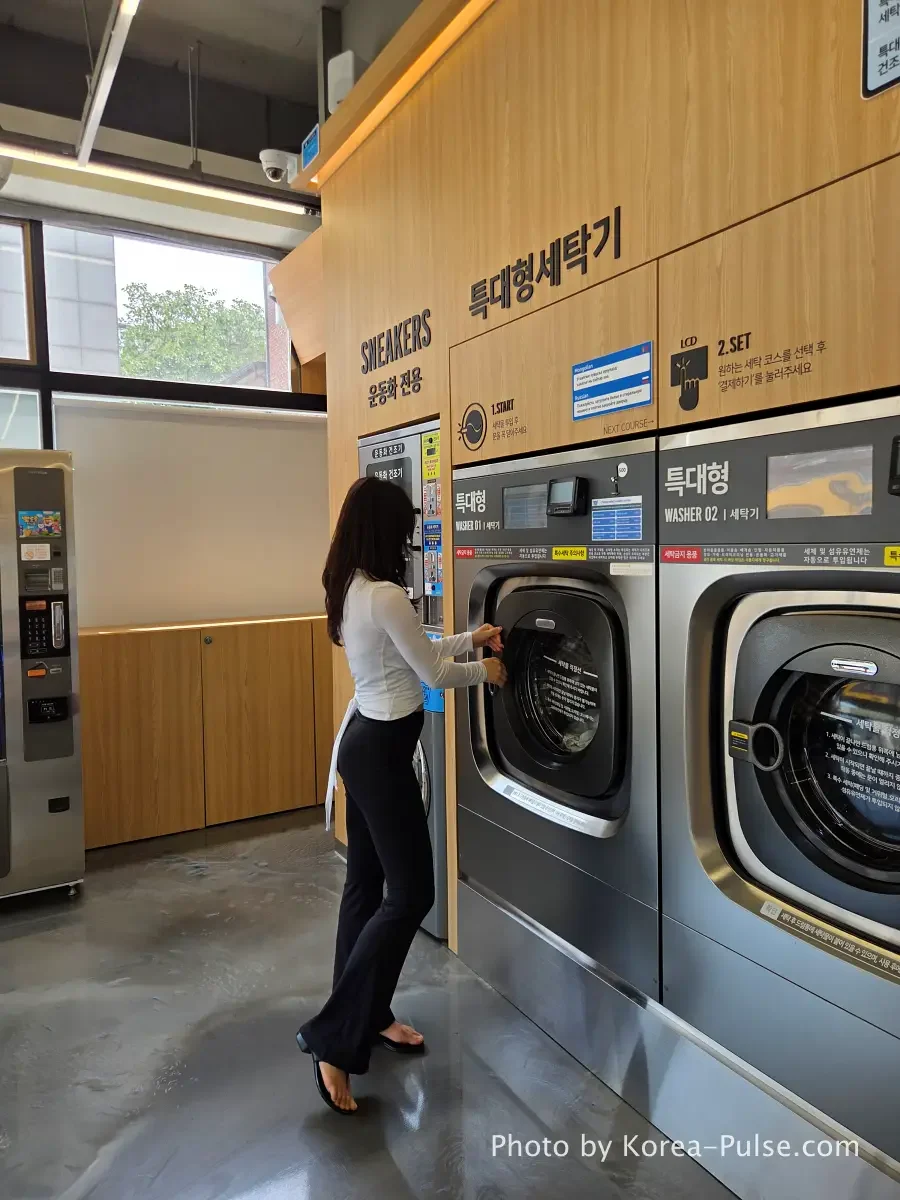 Woman standing in front of large industrial washing machines at Easy Wash modern coin laundry in Seoul Korea
