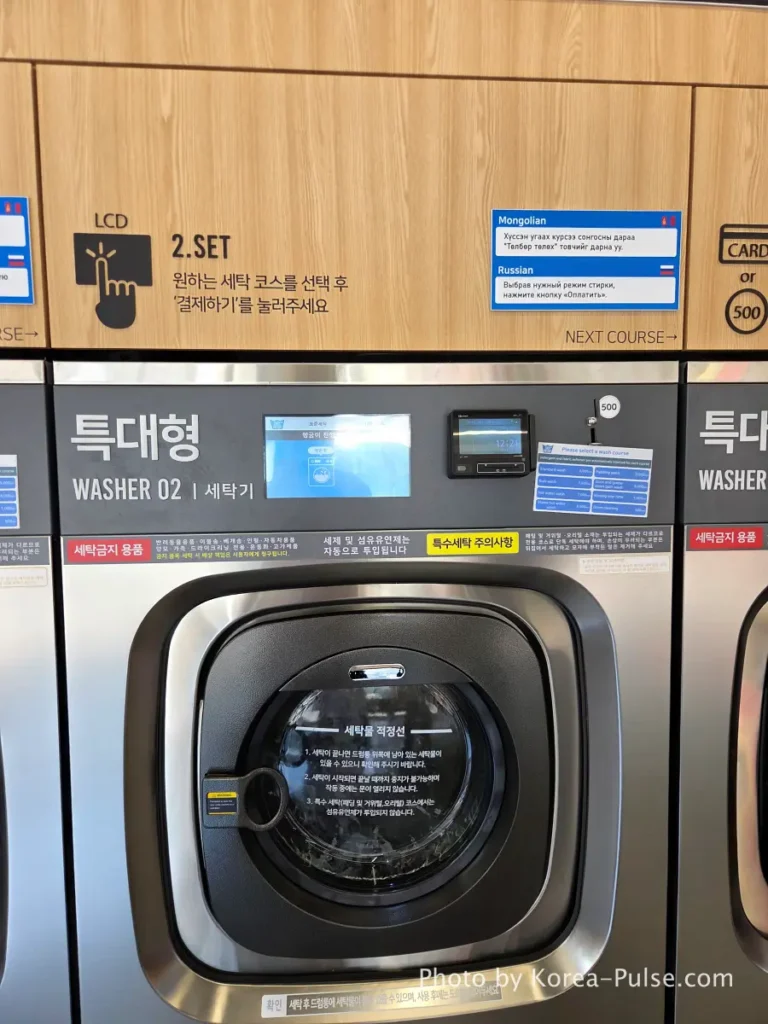 Close-up of washing machine drum door and digital touchscreen panel at Korean Easy Wash coin laundry showing wash cycle options in Korean