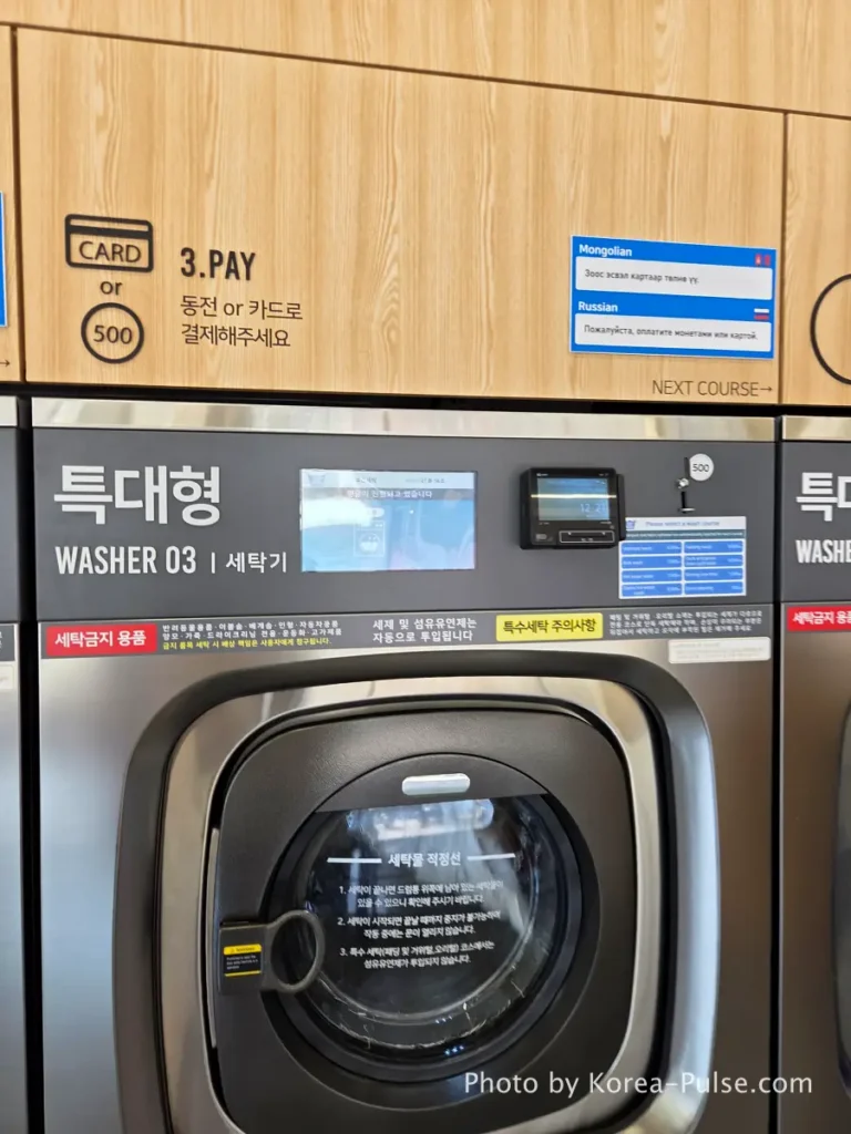 Credit card payment terminal on side of industrial washing machine at Easy Wash Korean coin laundry showing contactless tap payment