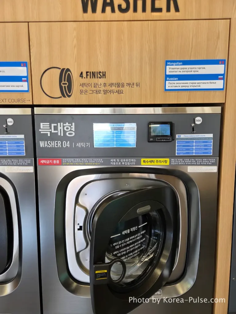 Open washing machine drum door at Easy Wash Korean coin laundry after cycle completed demonstrating the unwritten rule to leave door open after use