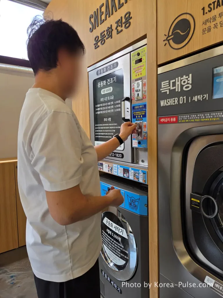 Man inserting 500 won coins into blue coin control panel on sneaker washing machine at Easy Wash Korean coin laundry Seoul