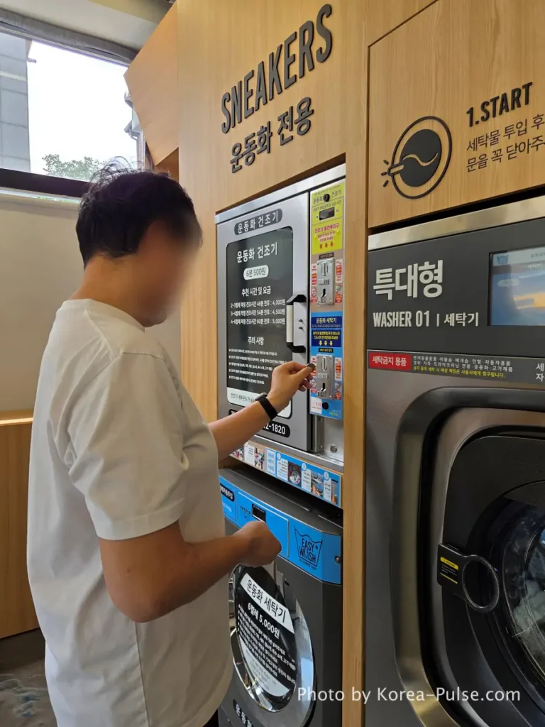 Close-up of blue coin slot upper panel on sneaker washing machine at Korean coin laundry showing 500 won coins being inserted