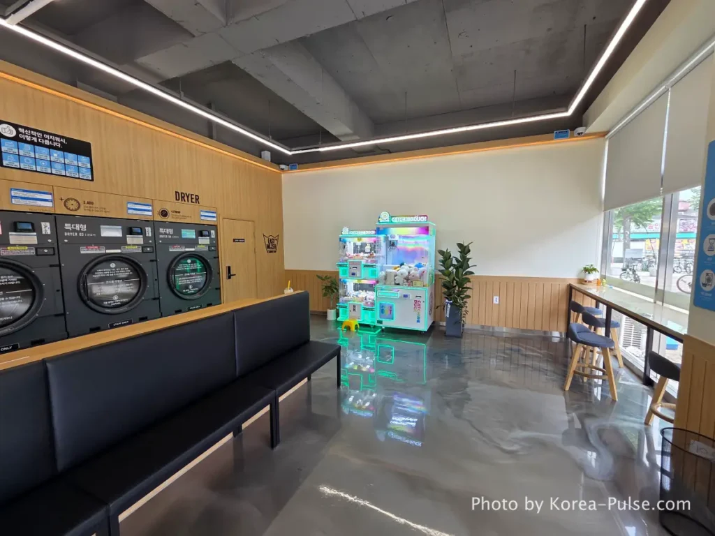 Interior right side of Easy Wash Korean coin laundromat showing rows of large commercial dryers and capsule toy gacha vending machine in corner