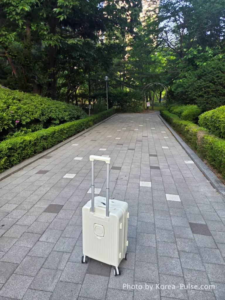 White carry-on suitcase standing upright on park pathway before Airport Bus 3300 trip from Ilsan