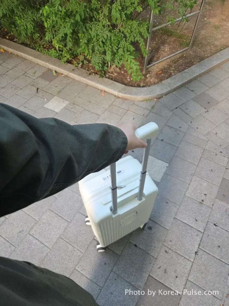 Hand pulling white carry-on suitcase along walkway on way to Airport Bus 3300 stop Ilsan