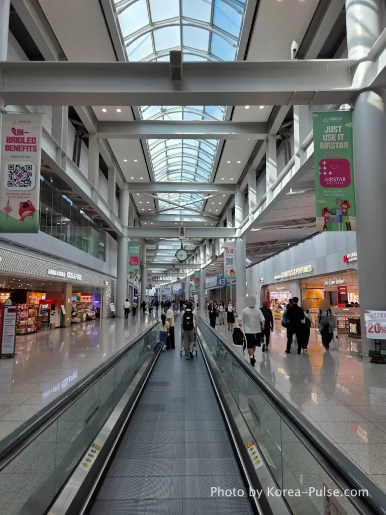 Incheon Airport Smartpass: Skip the Line & Hit the Lounge Fast 6 Incheon Airport Terminal 1 airside moving walkway with high glass ceiling and duty-free shops