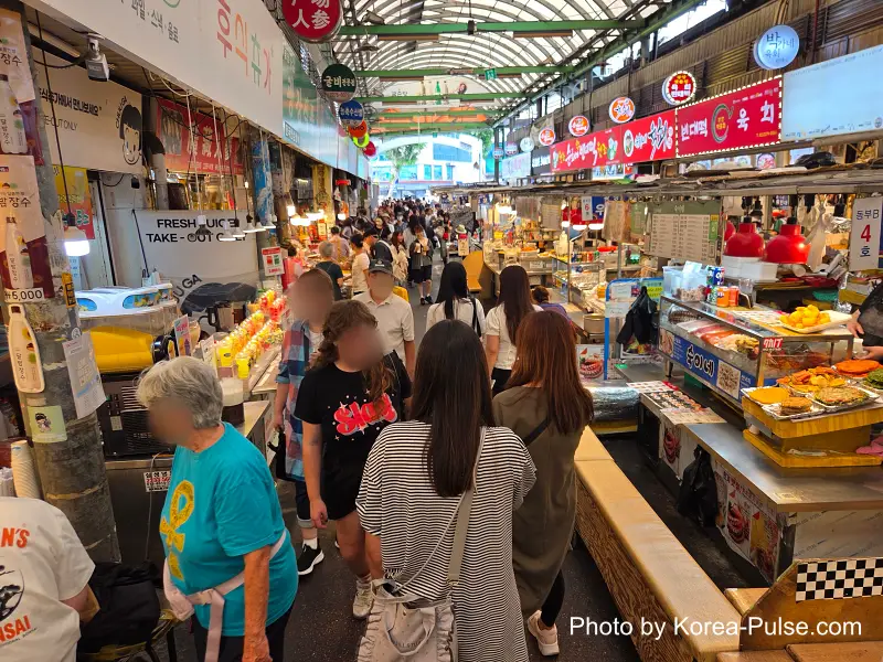 Gwangjang Market food alley toward North Gate 2 lined with stalls and lunchtime crowd both sides