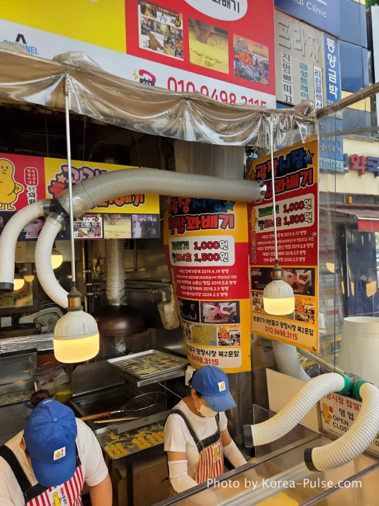 Gwangjang Market kkwabaegi price sign showing 1000 won kkwabaegi and 1500 won red bean donut with TV broadcast logos