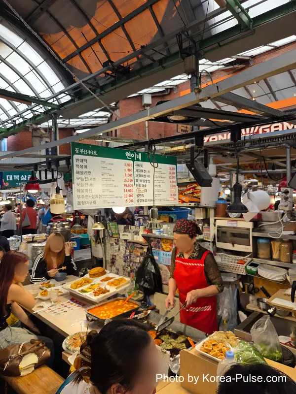 Gwangjang Market food alley multi-menu stall selling bindaetteok tteokbokki and Korean snack foods