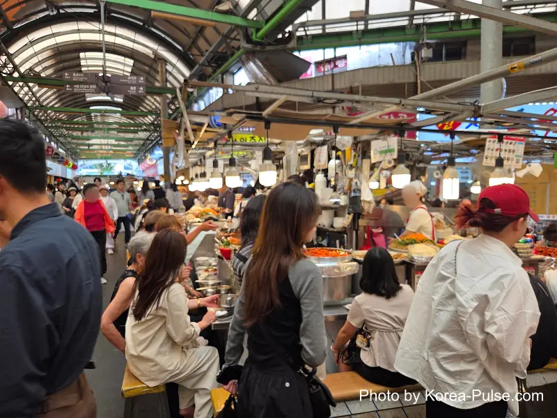 Gwangjang Market food alley central bench area packed with visitors eating dakbal sundae Korean street food
