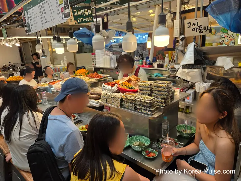 Foreign family eating gimbap and Korean snack foods at Gwangjang Market food alley bench