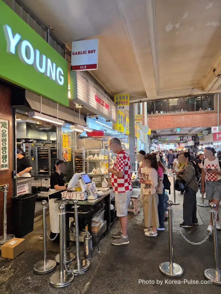 Garlic Boy Gwangjang Market foreign visitors queuing at counter with illuminated sign overhead
