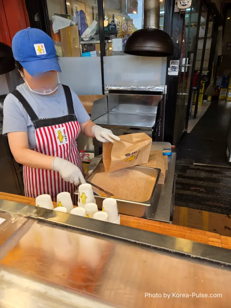 Gwangjang Market kkwabaegi staff rolling twisted donut in sugar before serving at counter