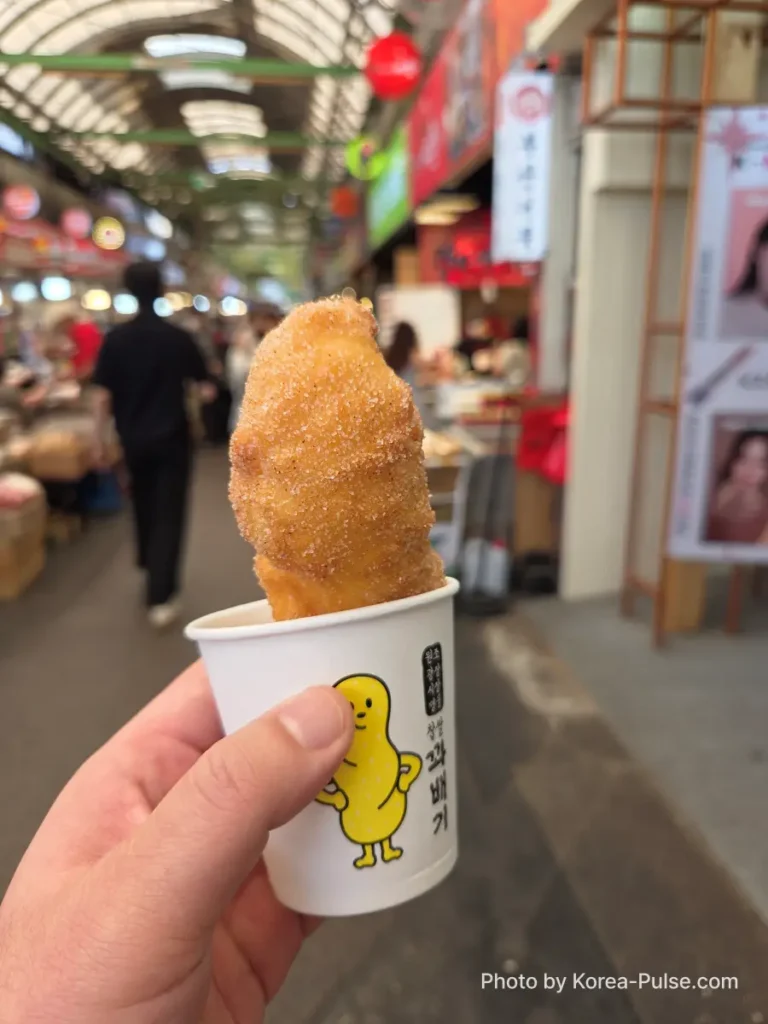 Gwangjang Market worth the wait — kkwabaegi twisted donut in paper cup held up at North Gate 2 Seoul