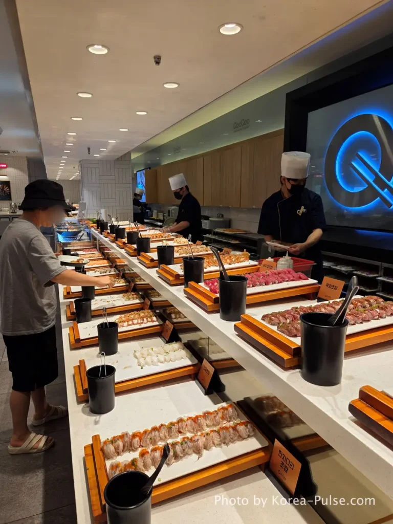 Long sushi counter with dozens of nigiri varieties at QooQoo Korean sushi buffet