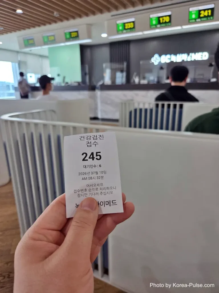 Hand holding a paper queue ticket numbered 245 at a health checkup reception kiosk