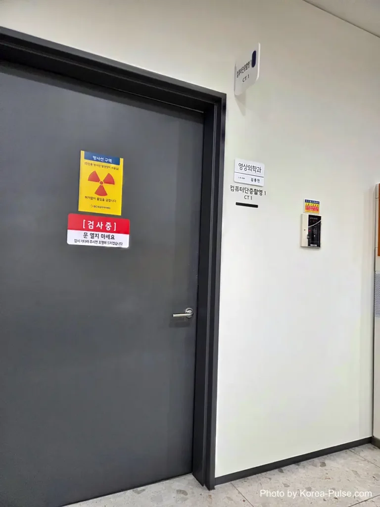Closed door marked with a yellow radiation warning sign outside a CT scan room