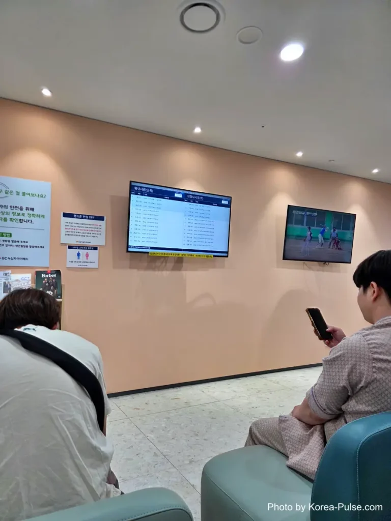 Crowded waiting room with a digital queue monitor listing patient names for the endoscopy department